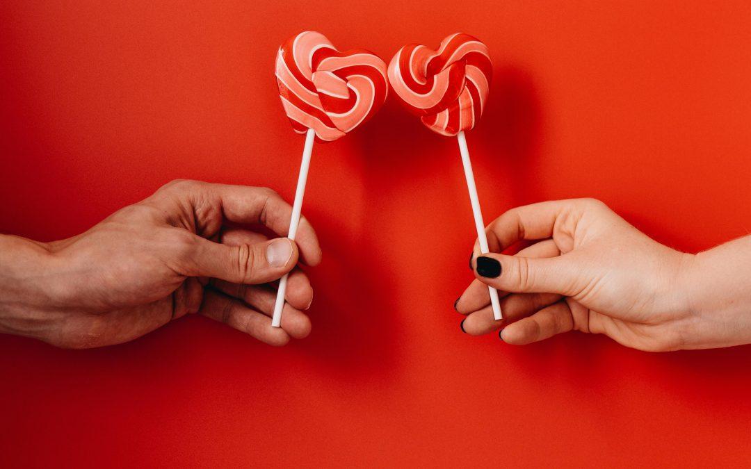 Två händer som håller hjärtformade klubbor mot en röd bakgrund – en söt och symbolisk gest för Alla hjärtans dag.